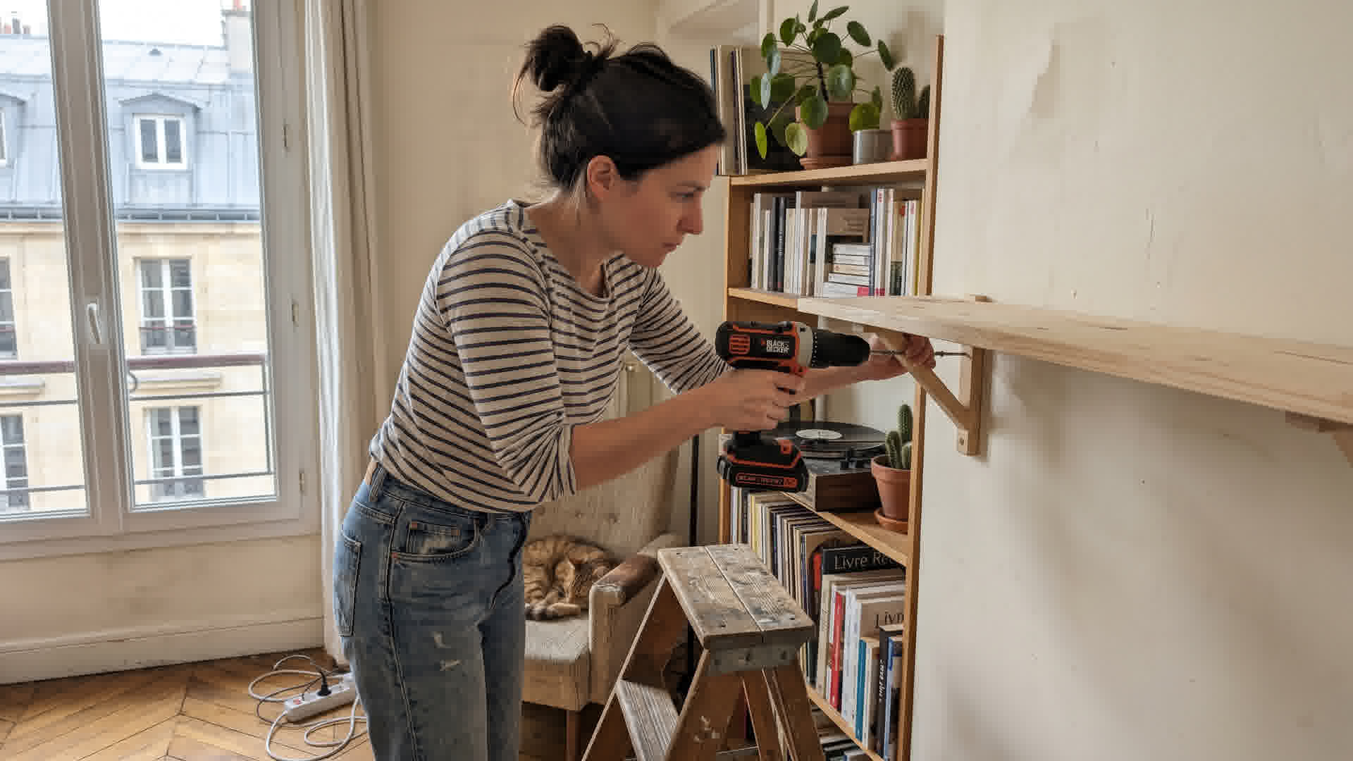 Personne utilisant une perceuse pour fixer une étagère dans un appartement français
