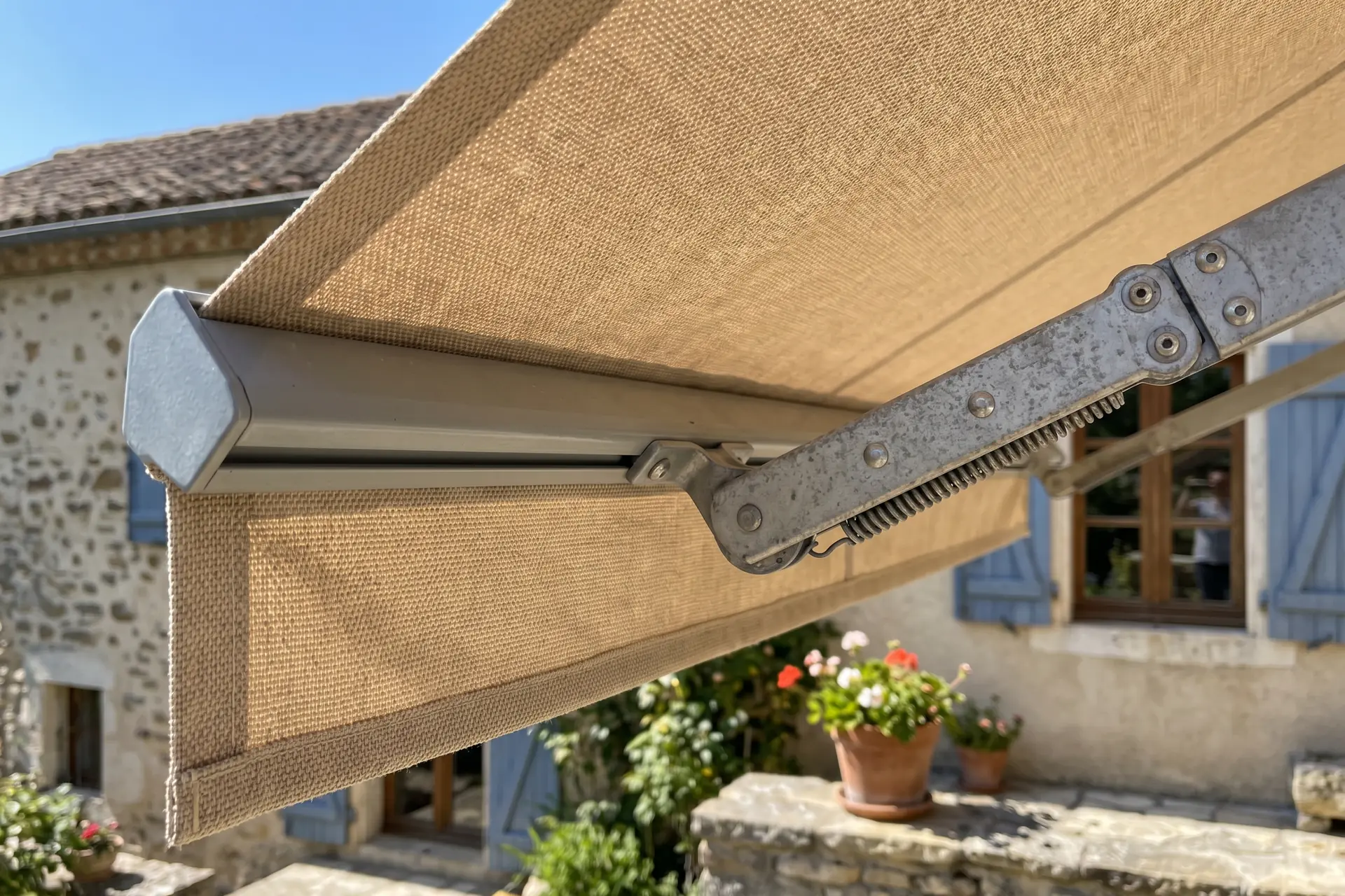 Gros plan sur une toile acrylique beige de store banne déployée sur bras articulé métallique